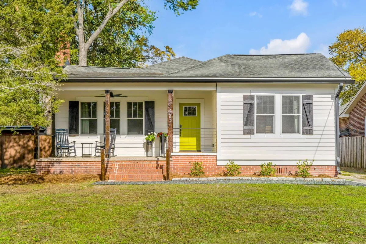 This image captures the home's bright yellow front door, traditional front porch, green lawn, and surrounding trees. The porch looks inviting and offers a glimpse of neighborhood life just outside the entry.