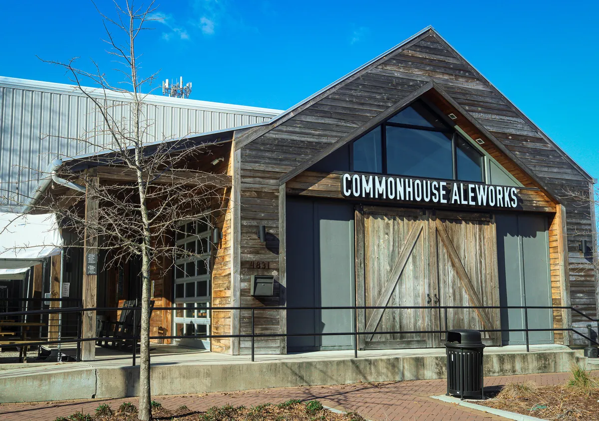 The photo shows a modern wooden facade with large glass windows and clear signage, featuring guests gathering and sampling craft beers. The atmosphere is communal and welcoming, hinting at the area's brewery scene.