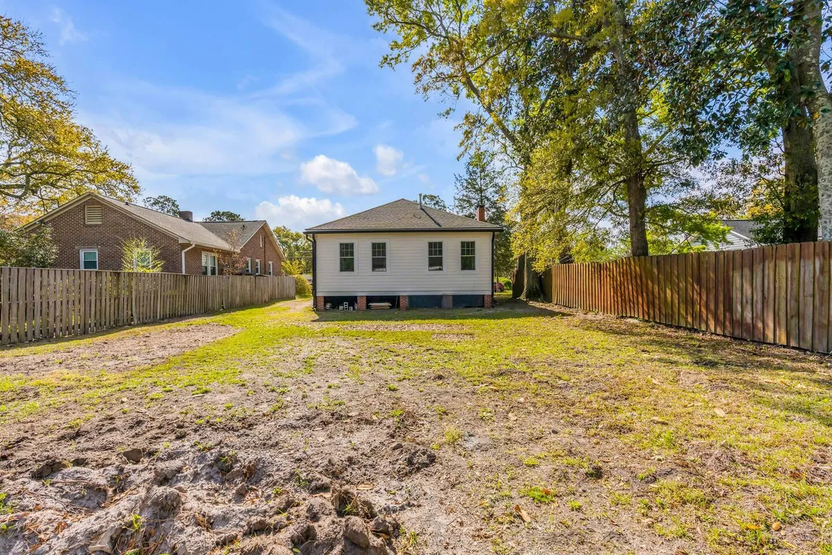 The image displays a charming single-story house surrounded by mature trees and a fenced yard, evoking a sense of privacy and tranquility. The inviting exterior suggests a peaceful retreat while being situated in a lively, walkable neighborhood.