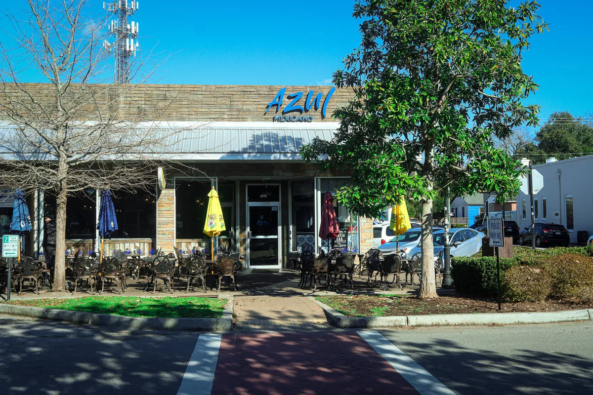 A lively exterior scene showcasing a restaurant with outdoor seating, decorative umbrellas, and lush greenery. The atmosphere is bustling and social, reflecting the energetic environment of Park Circle's dining scene.